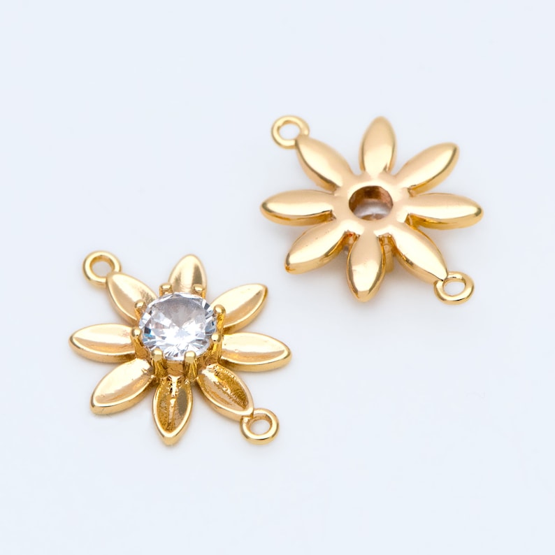 May include: Two gold-tone flower-shaped charms with a clear rhinestone in the center. One charm has two loops on the side, the other has one loop on the side.