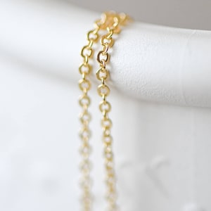 May include: Two gold chains, one slightly thicker than the other, are draped over a white surface. The chains are made of small, linked circles.