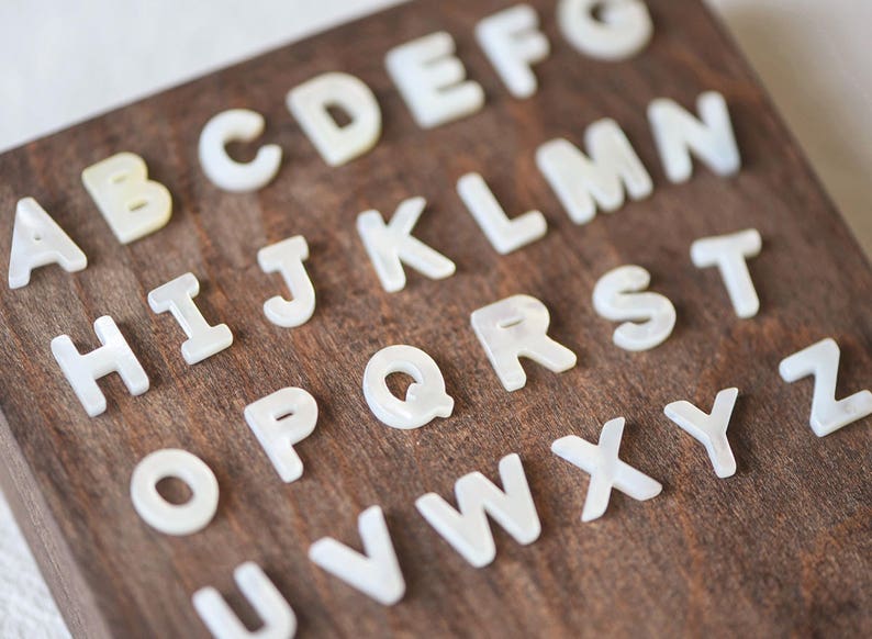May include: White plastic letters of the alphabet are arranged on a dark brown wooden surface. The letters are in alphabetical order.