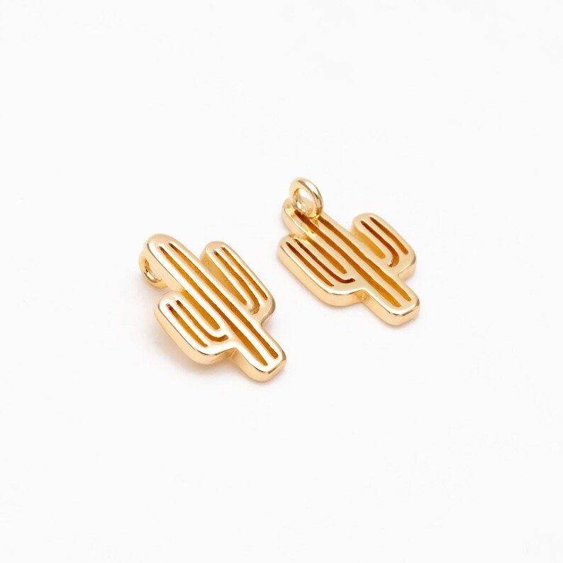 Op de afbeelding: Twee goudkleurige metalen cactusbedels met een lus om aan sieraden of andere knutselwerkjes te bevestigen.