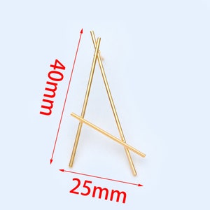 Puede incluir: Un expositor de metal dorado con forma triangular. El expositor mide 40 mm de alto y 25 mm de ancho.