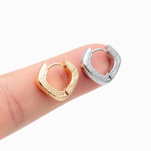 May include: Two square-shaped hoop earrings, one gold-toned and one silver-toned, are displayed. The earrings have a textured surface and a hinged closure. The earrings are shown on a white background.