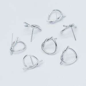 May include: Six silver knot earrings with a simple post design. The earrings are made of twisted metal and have a circular shape.