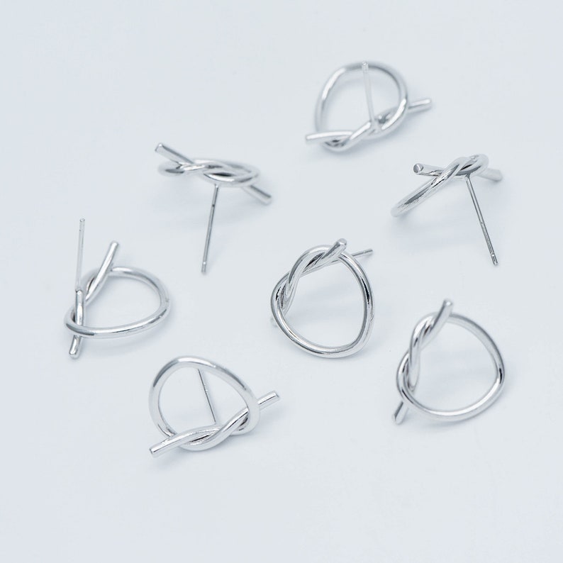 May include: Six silver knot earrings with a simple post design. The earrings are made of twisted metal and have a circular shape.