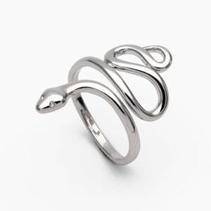 May include: A silver snake ring with a coiled design. The snake's head has two small, clear stones for eyes. The ring wraps around the finger, creating a unique accessory. The ring is set against a white background.