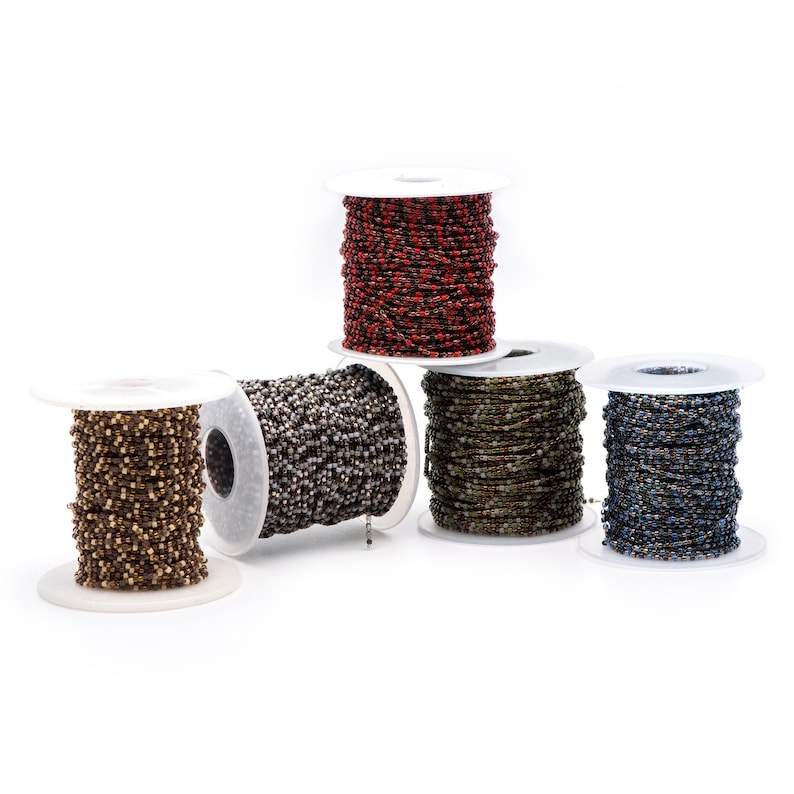May include: Five spools of beaded chain, each in a different color: red, silver, green, blue. The spools are on a white background.