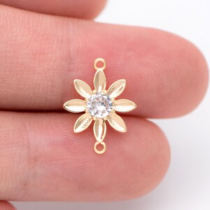 May include: Gold-tone flower charm with a clear rhinestone center. The charm has a loop on the top and bottom for attaching to jewelry.
