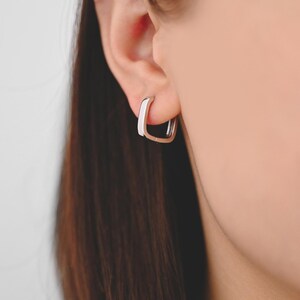 Pu&ograve; includere: Un paio di orecchini a cerchio quadrati in argento. Gli orecchini sono semplici ed eleganti e sarebbero un'ottima aggiunta a qualsiasi collezione di gioielli.