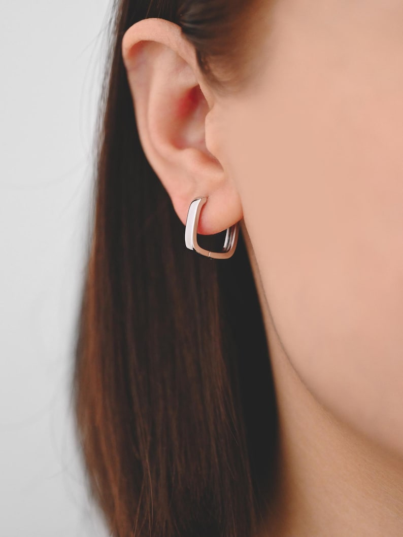 Pu&ograve; includere: Un paio di orecchini a cerchio quadrati in argento. Gli orecchini sono semplici ed eleganti e sarebbero un'ottima aggiunta a qualsiasi collezione di gioielli.