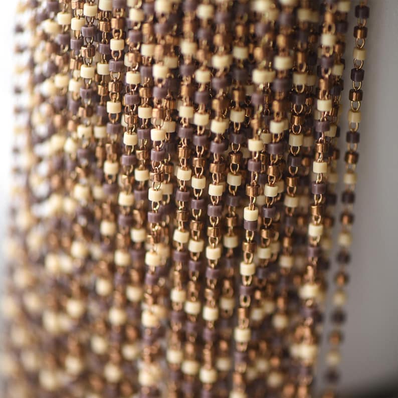 May include: A close-up of a chain made of small, brown and cream colored beads. The chain is made of metal and plastic beads.