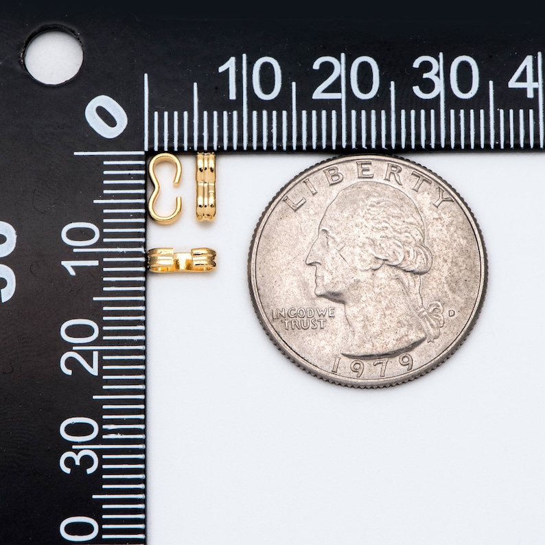 May include: Two gold-colored metal clasps for jewelry making, next to a US quarter for size comparison.  The clasps are about 1/2 inch long.