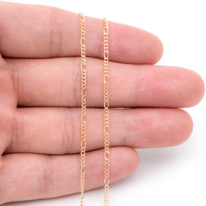 May include: A gold chain necklace with a delicate, fine-link design. The chain is shown on a hand, with the ends of the chain hanging down.