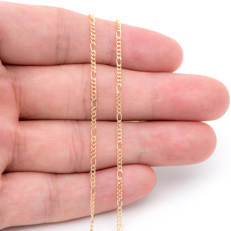 May include: A gold chain necklace with a delicate, fine-link design. The chain is shown on a hand, with the ends of the chain hanging down.