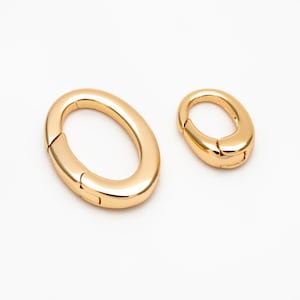 以下が含まれることがあります： 2つの金色の楕円形の留め具。片方はもう片方より大きい。滑らかで磨かれた仕上げです。