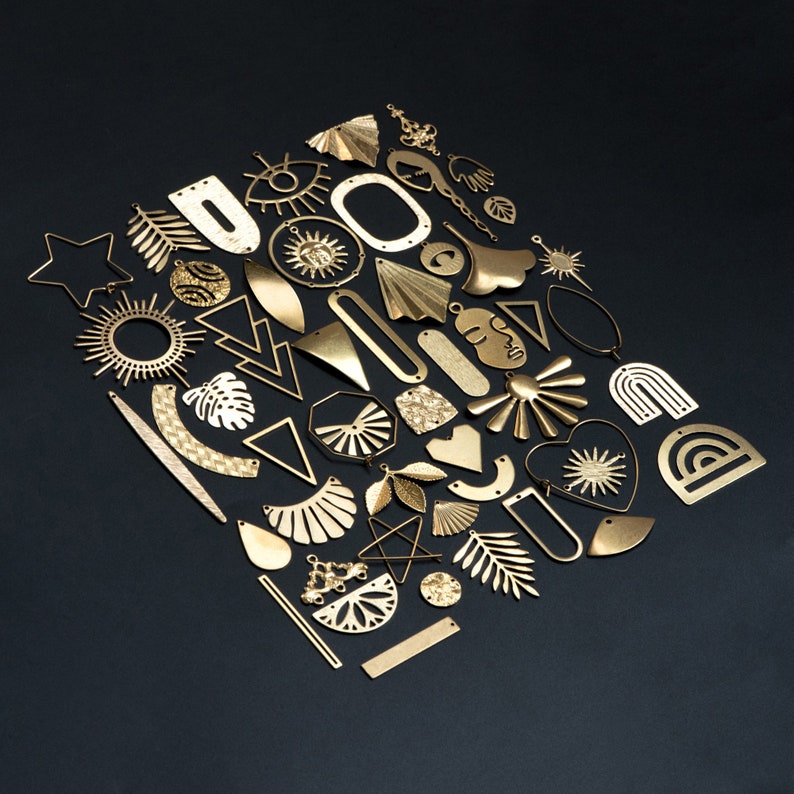 May include: A collection of gold-toned metal charms in various shapes, including stars, suns, hearts, and geometric designs. The charms are arranged in a pattern on a black background.