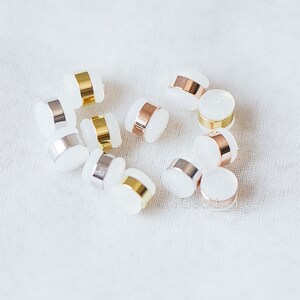 May include: A collection of white round beads with gold, silver, and rose gold metal accents. The beads are arranged on a white fabric surface.