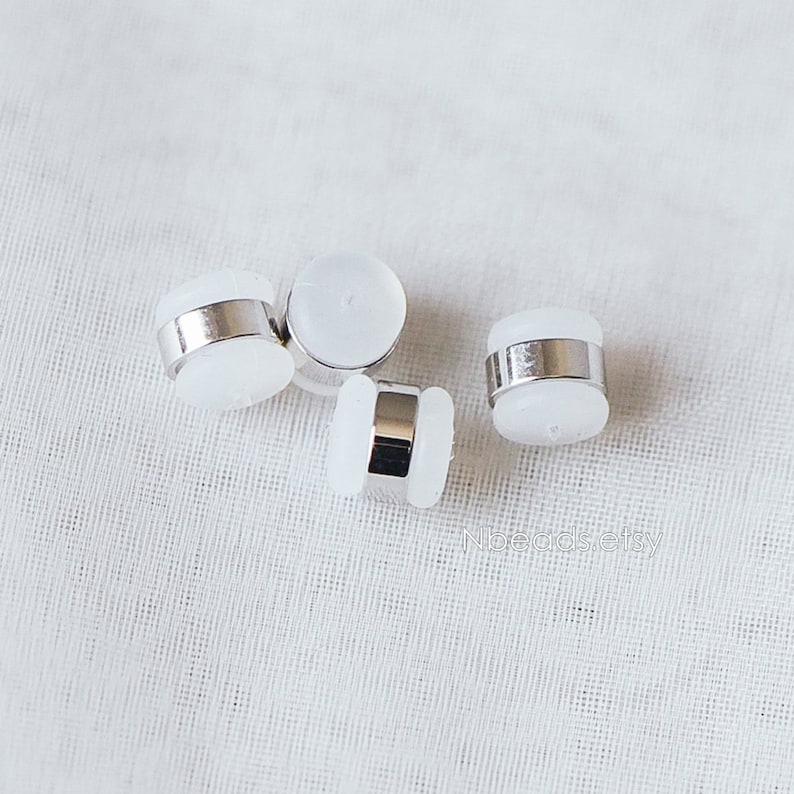 May include: Four white and silver round button-like objects with a silver band around the middle.