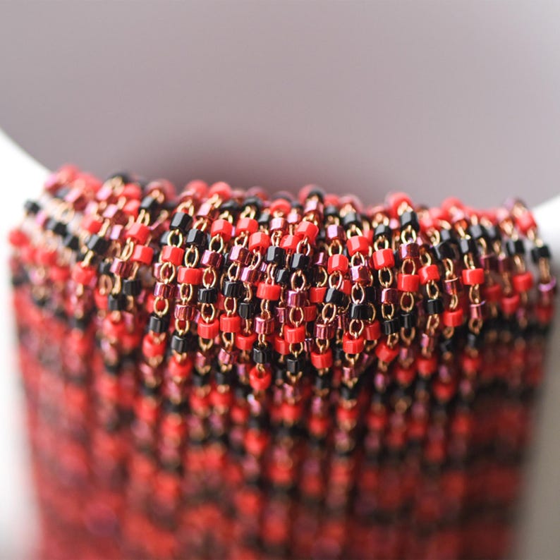 May include: Close-up of a red, black, and gold beaded chain. The chain is made of small, square beads that are strung together in a repeating pattern.