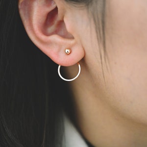 May include: A pair of gold earrings with a small ball stud and a larger hoop that hangs from the earlobe.