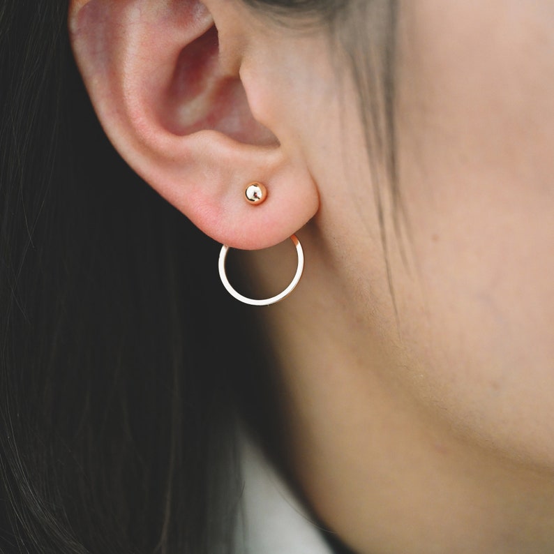 May include: A pair of gold earrings with a small ball stud and a larger hoop that hangs from the earlobe.