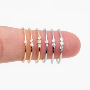 May include: Four dainty rings with three small diamonds each. Two rings are gold and two are silver.