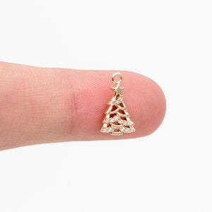 Puede incluir: Encanto de árbol de Navidad de tono dorado con diamantes de imitación transparentes y una estrella en la parte superior.