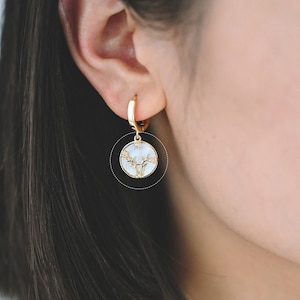May include: Gold hoop earrings with a white, round charm featuring a gold deer silhouette.