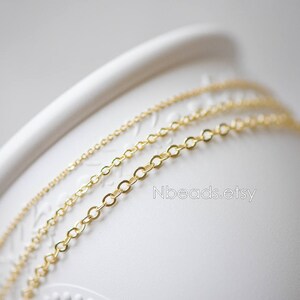 May include: Three gold chains of different sizes and thicknesses are displayed on a white surface. The chains are arranged in a layered pattern, with the largest chain on the bottom and the smallest chain on top.