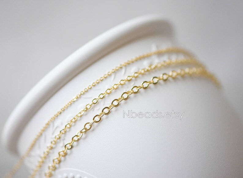 May include: Three gold chains of different sizes and thicknesses are displayed on a white surface. The chains are arranged in a layered pattern, with the largest chain on the bottom and the smallest chain on top.