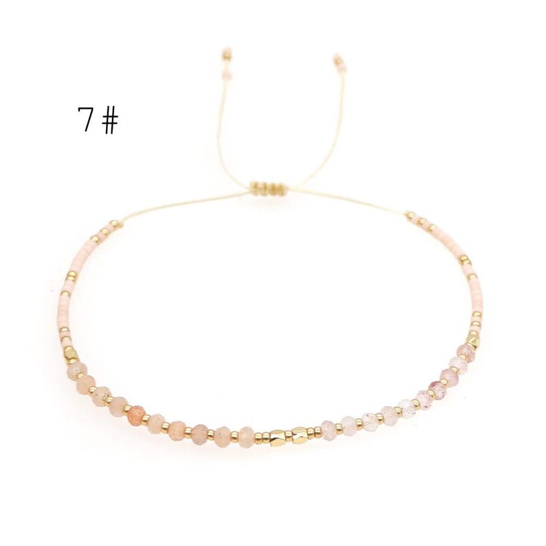May include: A delicate pink and gold beaded bracelet with a sliding knot closure. The bracelet features small, round beads in shades of pink and gold, with a single gold bead accent.