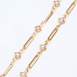 May include: A gold chain necklace with small white pearls set in square frames. The chain is made of linked rectangular pieces.
