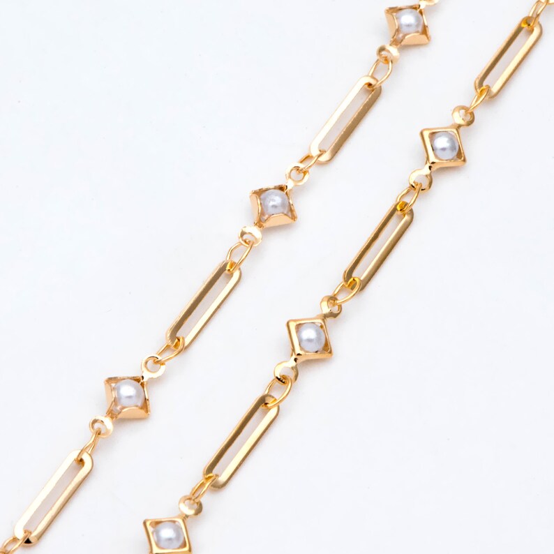 May include: A gold chain necklace with small white pearls set in square frames. The chain is made of linked rectangular pieces.