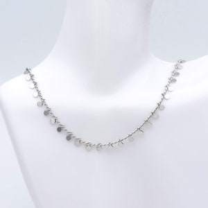 May include: A silver necklace with a delicate chain and small, round silver charms hanging from it.
