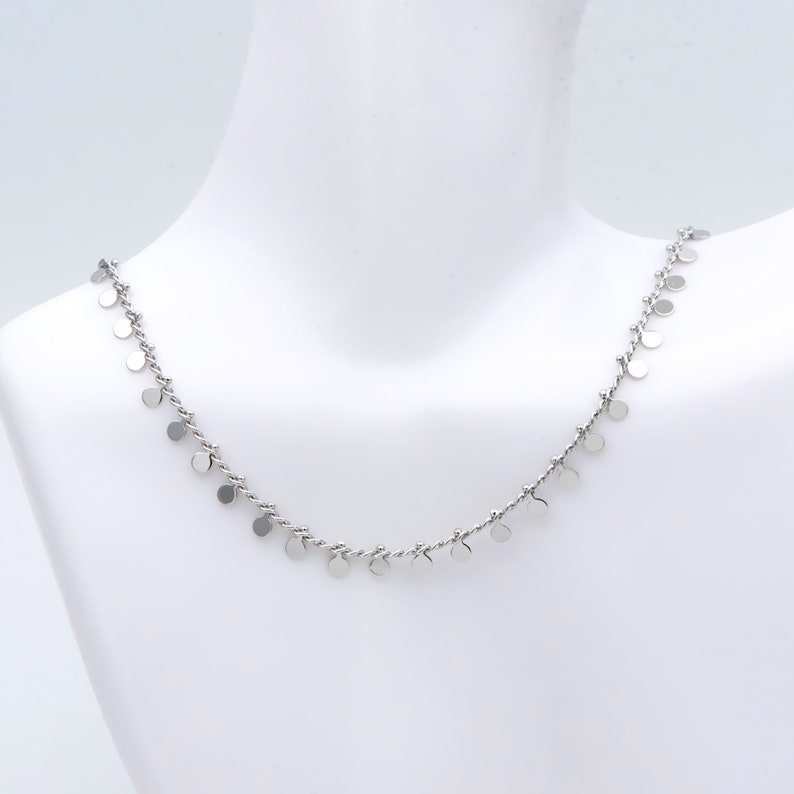 May include: A silver necklace with a delicate chain and small, round silver charms hanging from it.