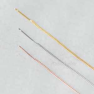 Könnte beinhalten: Drei zarte Ketten in Gold, Silber und Roségold. Die Ketten sind dünn und haben ein zartes, verlinktes Design. Sie liegen horizontal auf einer weißen Oberfläche.