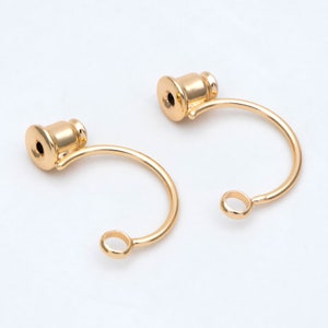 May include: Two gold-toned earring hoops with a small, round loop at the bottom and a decorative, cylindrical top.