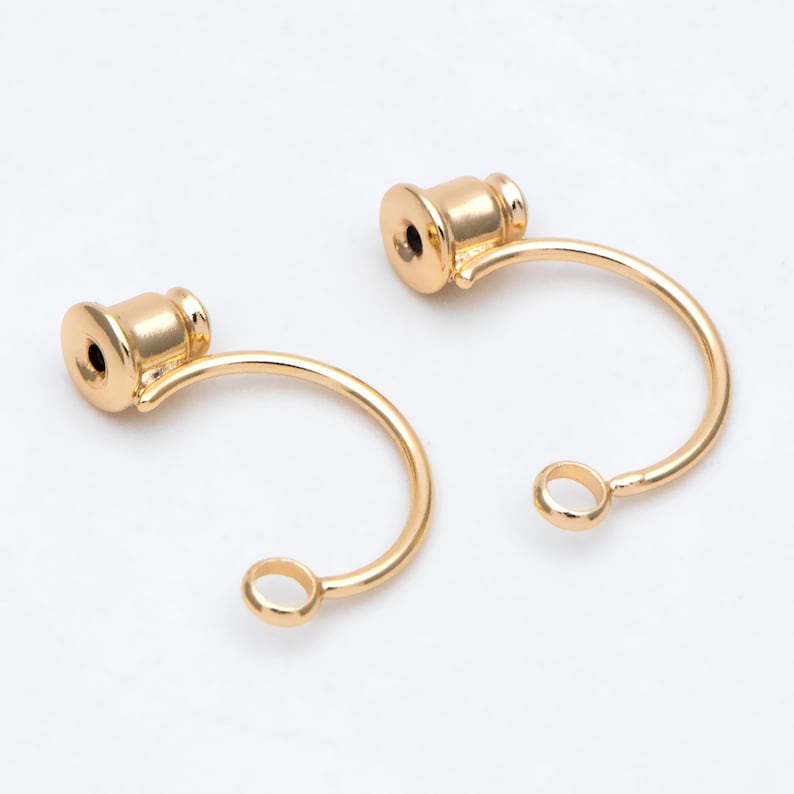 May include: Two gold-toned earring hoops with a small, round loop at the bottom and a decorative, cylindrical top.