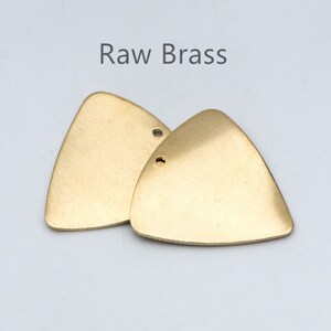 Könnte beinhalten: Zwei rohe Messing-Dreiecksformen mit einem Loch in jeder. Der Text "Raw Brass" steht über den Formen.