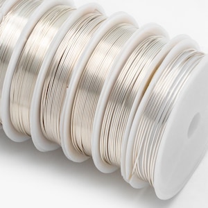 May include: Close-up of spools of silver-colored wire. The wire is wound around white spools.