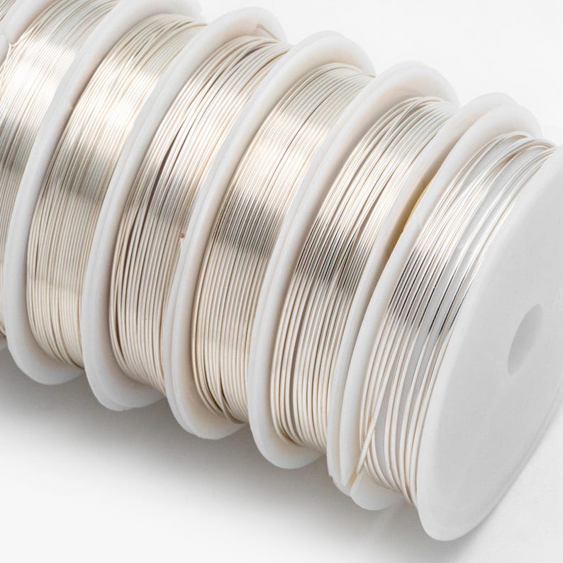 May include: Close-up of spools of silver-colored wire. The wire is wound around white spools.