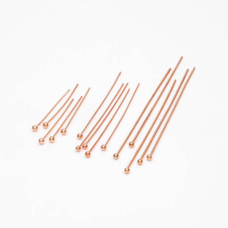 May include: A set of 15 gold-toned head pins with rounded tips. The pins are arranged in rows of varying lengths.