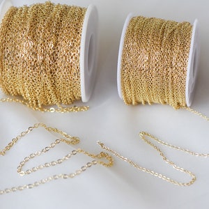 May include: Two spools of gold chain, one larger than the other, with a length of chain extending from each spool. The chain is a delicate, fine link style.