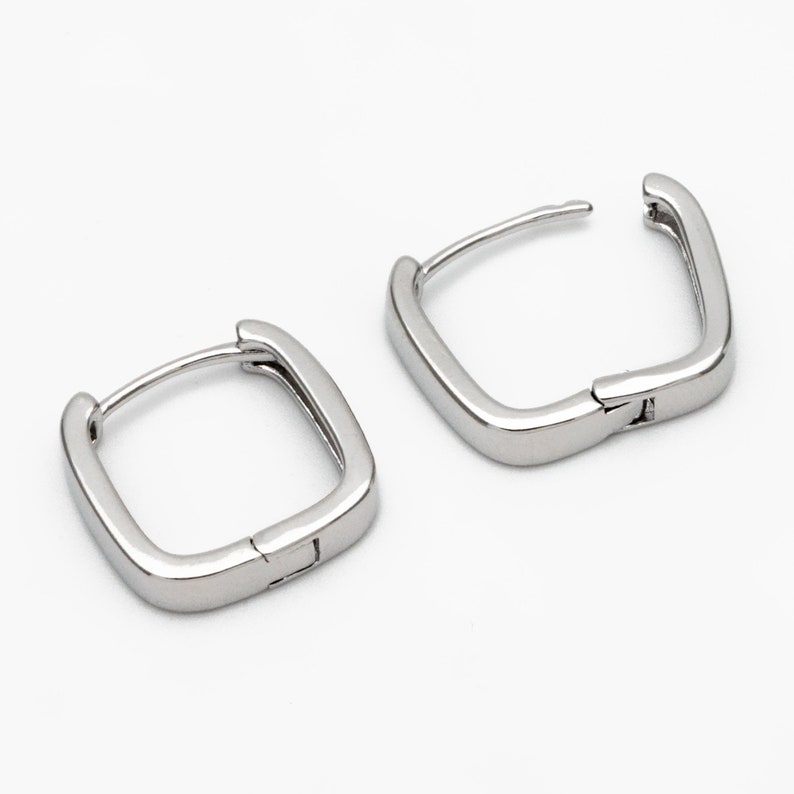 Pu&ograve; includere: Un paio di orecchini a cerchio quadrati in argento. Gli orecchini sono in metallo e hanno una chiusura a cerniera.