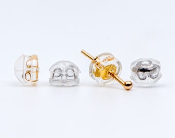 May include: Three clear plastic earring backs, one with a gold post. The backs are designed to hold earrings in place.