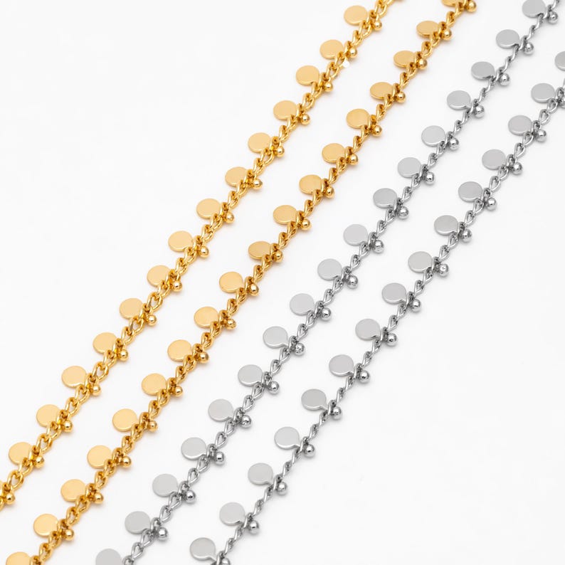 May include: Two chains with small round gold and silver charms hanging from them. The chains are on a white background.