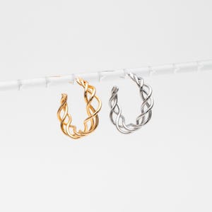 May include: Two pairs of hoop earrings, one gold and one silver, with a braided design.