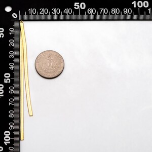 May include: Two gold chains, each approximately 5 cm long, are laid out next to a US quarter. The chains are flat and have a slightly textured surface.
