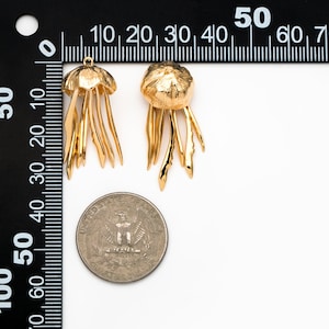 May include: Two gold-colored jellyfish earrings with detailed tentacles. The earrings are shown next to a US quarter for size comparison.
