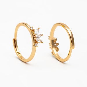 May include: Two gold rings with clear crystal accents. The ring on the left has a larger crystal design and the ring on the right has a smaller crystal design.