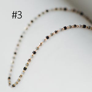 May include: A delicate gold chain necklace with small square-shaped beads in black, gray, and white.